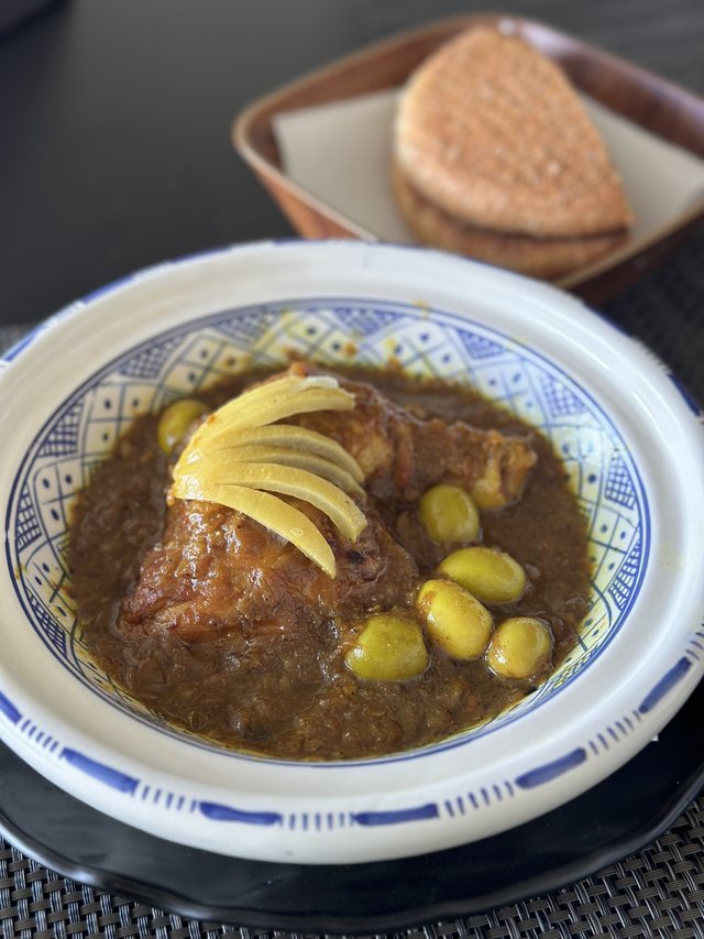 Tajine de poulet au citron confit et aux olives vertes, servi dans un plat en céramique bleue avec du pain